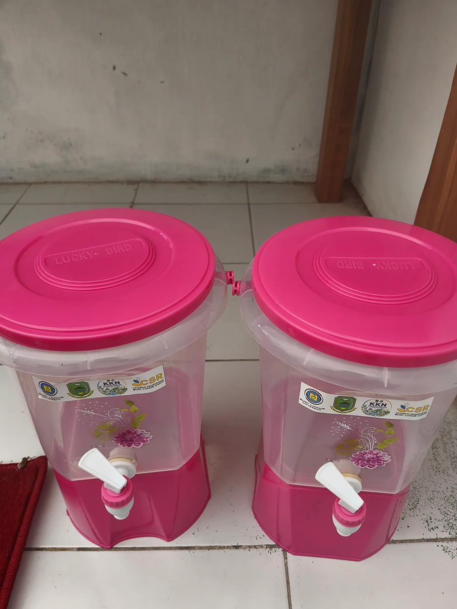 Dua dispenser non-listrik berwarna merah muda dengan keran untuk TK Al-Hidayah.