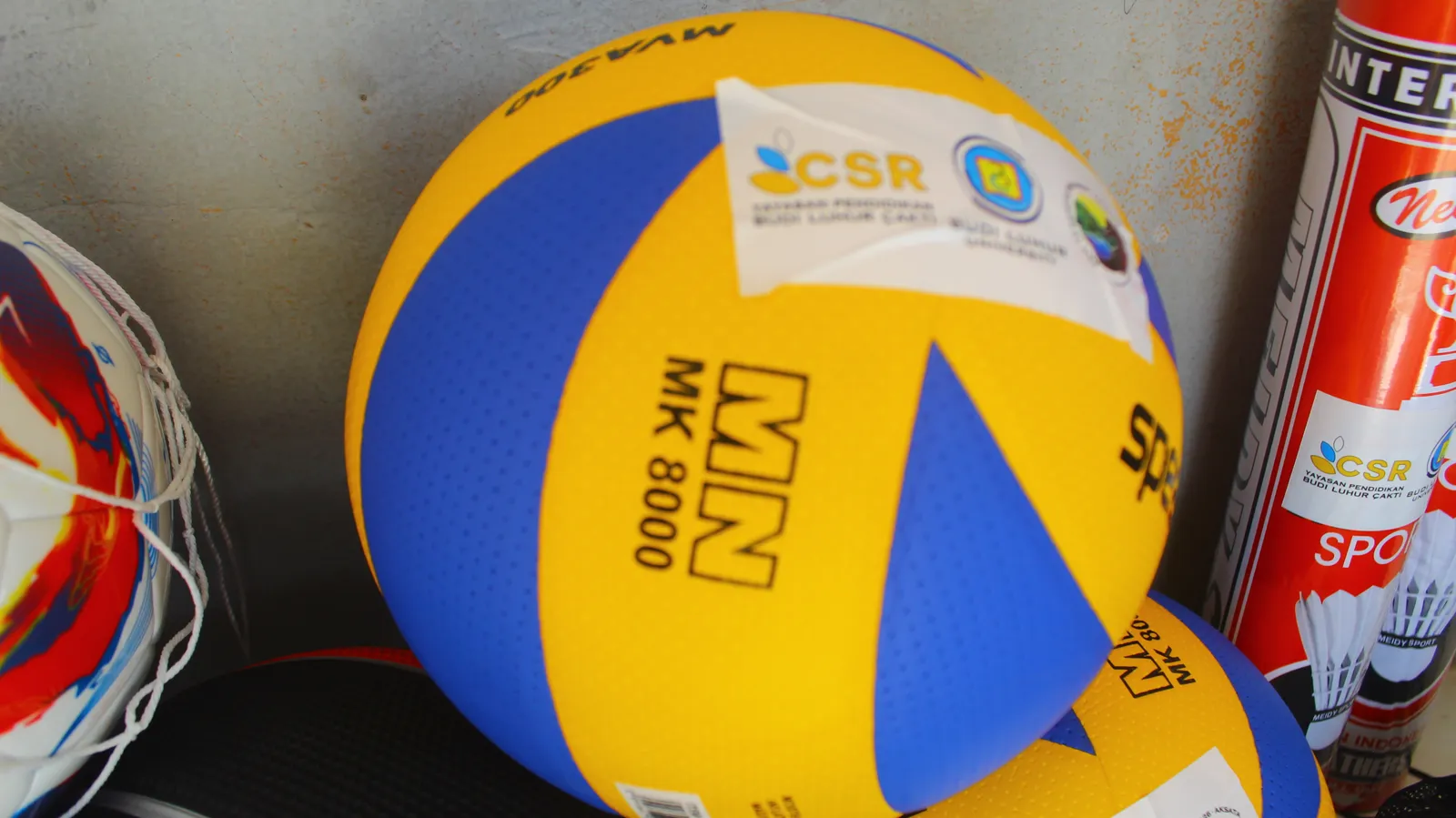 Dua bola voli kuning dan biru berlabel CSR diletakkan bersama perlengkapan olahraga.