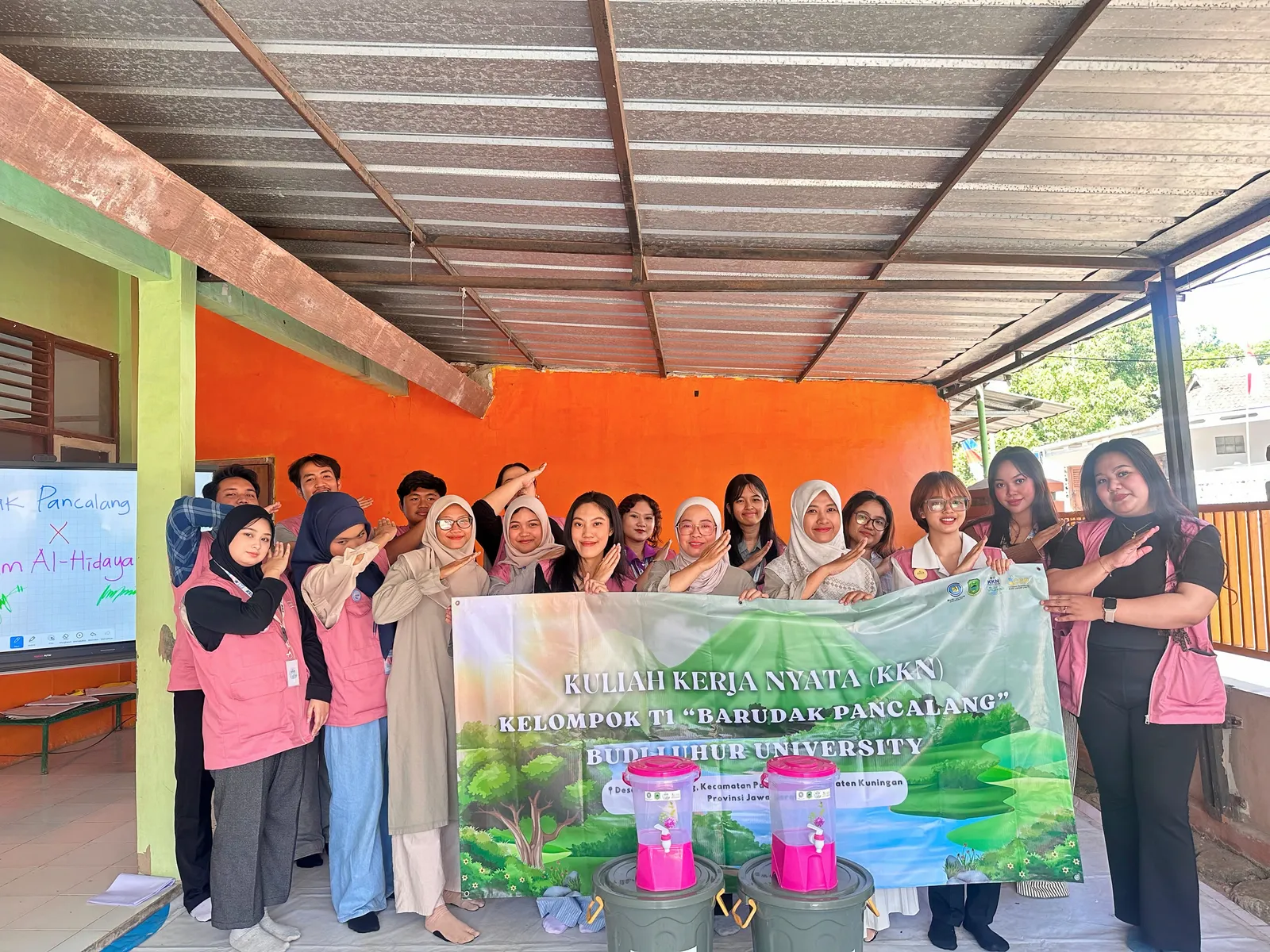 Tim KKN T1 dan pihak TK Al-Hidayah berfoto bersama dua tong keran air dan dua dispenser.