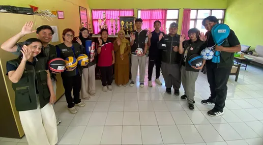 Tim KKN T3 dan pihak sekolah berfoto bersama sambil memegang berbagai alat olahraga.
