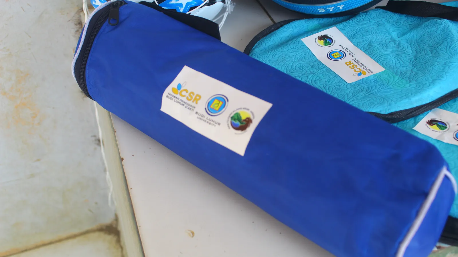 Tas biru berisi net voli berlabel CSR diletakkan bersama tas perlengkapan olahraga.