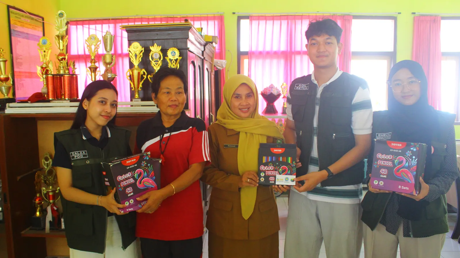 Tim KKN T3 berfoto bersama pihak sekolah sambil memegang paket pensil warna.