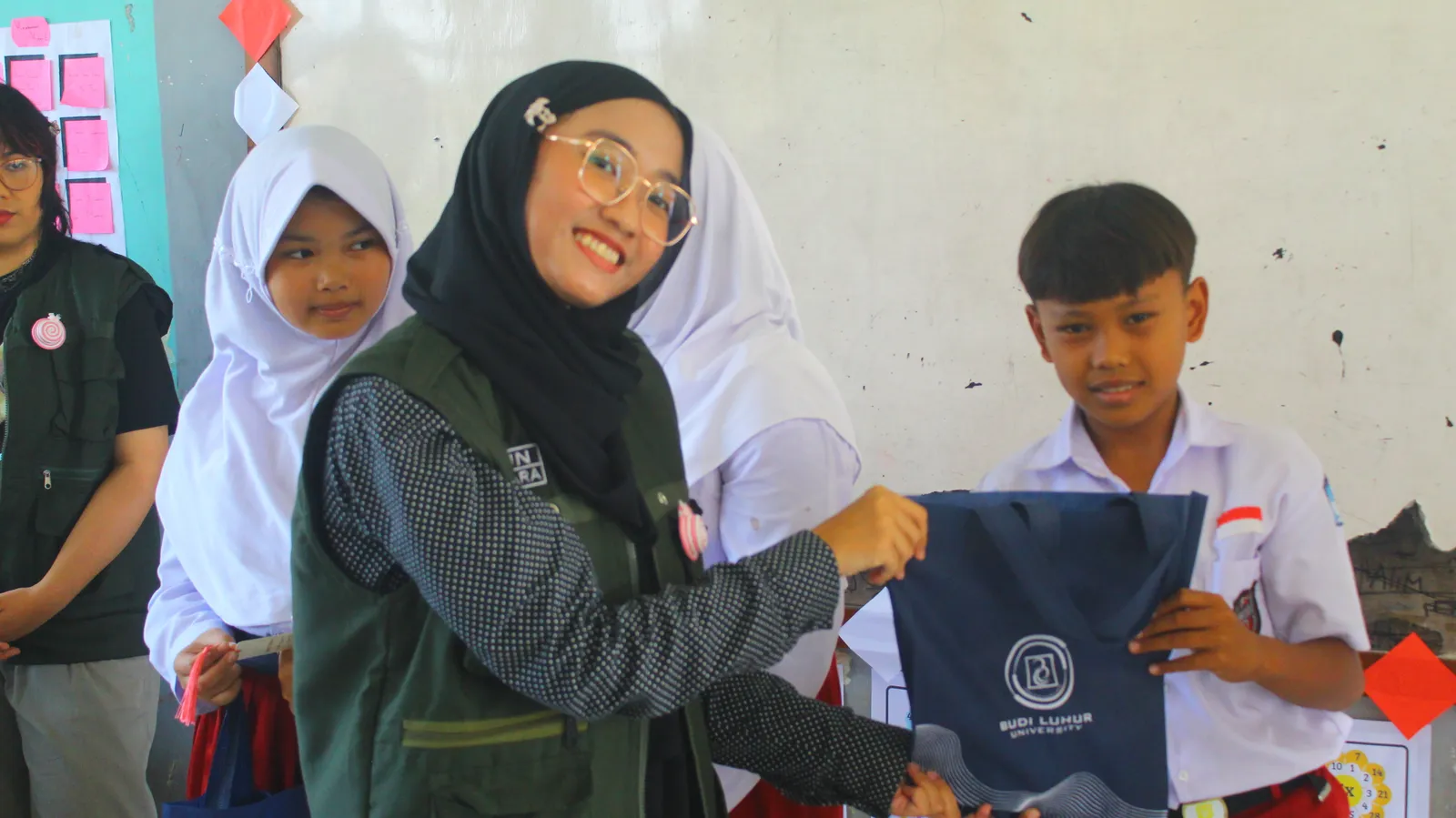 Anggota Tim KKN T3 menyerahkan tas suvenir kepada seorang siswa di depan kelas.